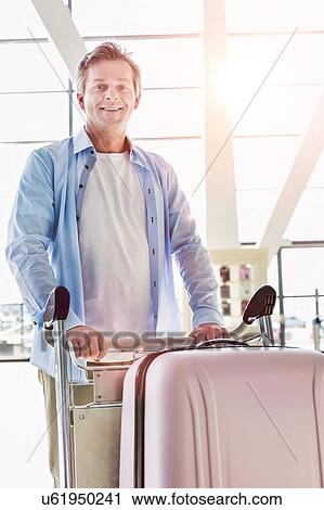 Portrait of mature attractive man pushing cart with his suitcase for check in at airport View Large Photo Image Stock Image - Portrait of mature attractive man pushing cart with his suitcase for check in at airport. Fotosearch