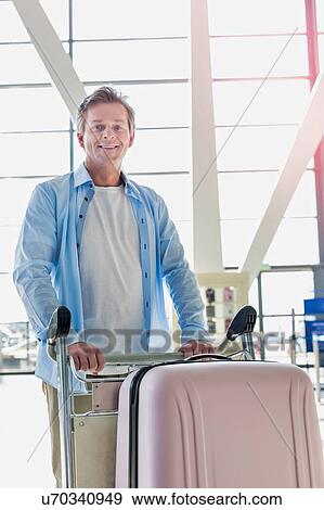 Stock Photo - Portrait of mature attractive man pushing cart with his suitcase for check in at airport. Fotosearch