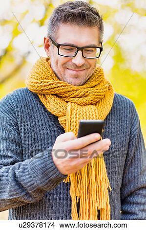 Picture - Portrait of mature attractive man using smartphone under maple tree in park. Fotosearch