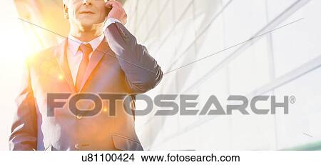 Picture - Portrait of mature attractive businessman talking on smartphone while standing at Gdansk Airport. Fotosearch
