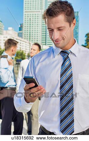 Stock Image - Portrait of mature attractive businessman smiling while using smartphone after work. Fotosearch