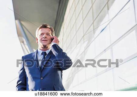 Stock Image - Portrait of mature attractive businessman talking on smartphone while standing at Gdansk Airport. Fotosearch