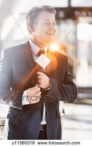 Stock Photo - Portrait of mature attractive businessman taking out his passport from his suit in airport. Fotosearch