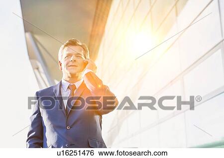 Stock Photograph - Portrait of mature attractive businessman talking on smartphone while standing at Gdansk Airport. Fotosearch