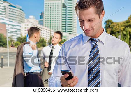 Stock Photography - Portrait of mature attractive businessman smiling while using smartphone after work. Fotosearch