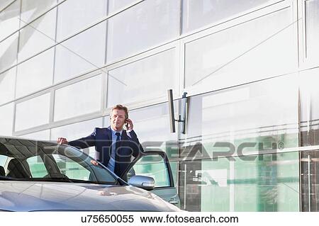 Stock Photography - Portrait of mature attractive businessman talking on smartphone while standing outside the car. Fotosearch
