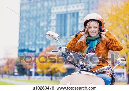 Stock Photo - Portrait of mature beautiful woman putting her helmet on to ride motorbike in park. Fotosearch