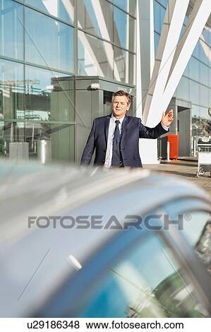 Stock Photo - Portrait of mature businessman calling taxi in the airport. Fotosearch