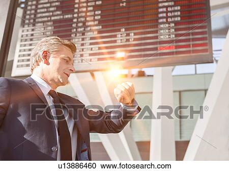 Stock Image - Portrait of mature businessman checking time on his watch while waiting in the airport. Fotosearch