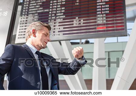 Stock Photography - Portrait of mature businessman checking time on his watch while waiting in the airport. Fotosearch