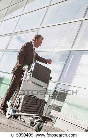 Portrait of mature businessman checking time on his watch while waiting in the airport View Large Photo Image Stock Photography - Portrait of mature businessman checking time on his watch while waiting in the airport. Fotosearch