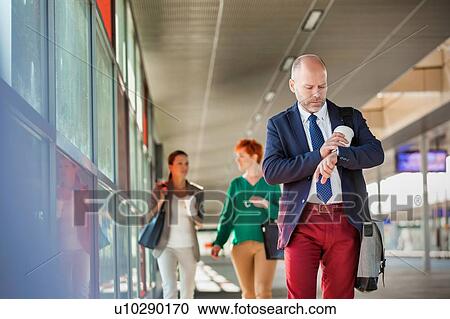 Stock Image - Portrait of mature businessman holding a cup of coffee while looking at his watch. Fotosearch