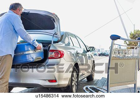 Portrait of mature businessman putting his luggage on car trunk with lens flare View Large Photo Image Picture - Portrait of mature businessman putting his luggage on car trunk with lens flare . Fotosearch