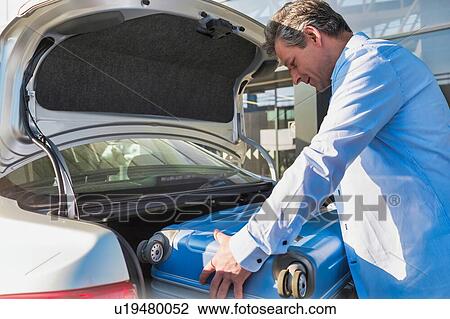 Stock Image - Portrait of mature businessman putting his luggage on car trunk with lens flare . Fotosearch