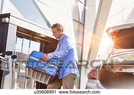 Portrait of mature businessman putting his luggage on car trunk with lens flare View Large Photo Image Stock Image - Portrait of mature businessman putting his luggage on car trunk with lens flare . Fotosearch