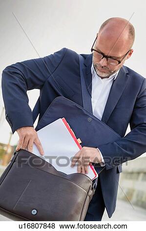 Portrait of mature businessman putting paperwork on his bag View Large Photo Image Stock Photo - Portrait of mature businessman putting paperwork on his bag. Fotosearch