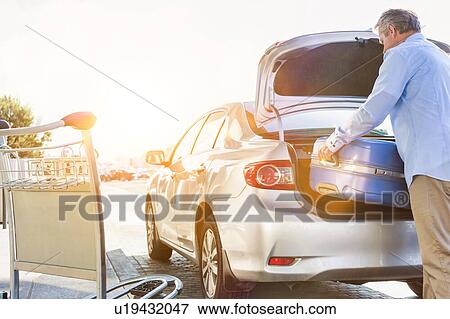 Portrait of mature businessman putting his luggage on car trunk with lens flare View Large Photo Image Stock Photo - Portrait of mature businessman putting his luggage on car trunk with lens flare . Fotosearch