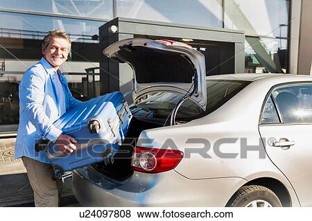 Portrait of mature businessman putting his luggage on car trunk with lens flare View Large Photo Image Stock Photo - Portrait of mature businessman putting his luggage on car trunk with lens flare . Fotosearch