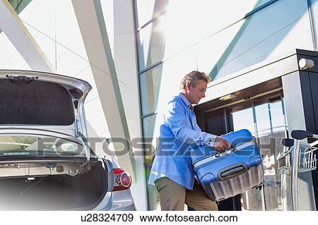 Stock Photo - Portrait of mature businessman putting his luggage on car trunk with lens flare . Fotosearch