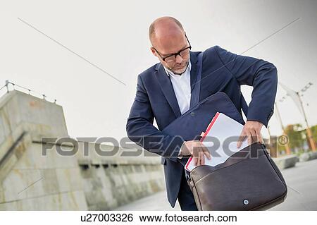 Portrait of mature businessman putting paperwork on his bag View Large Photo Image Stock Photograph - Portrait of mature businessman putting paperwork on his bag. Fotosearch