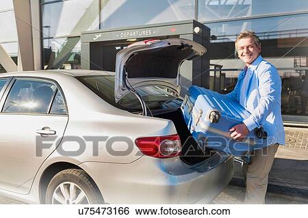 Portrait of mature businessman putting his luggage on car trunk with lens flare View Large Photo Image Stock Photograph - Portrait of mature businessman putting his luggage on car trunk with lens flare . Fotosearch