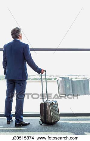 Portrait of mature businessman standing with his suitcase while looking through the window in airport View Large Photo Image Picture - Portrait of mature businessman standing with his suitcase while looking through the window in airport. Fotosearch