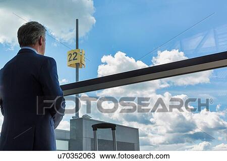Stock Image - Portrait of mature businessman standing with his suitcase while looking through the window in airport. Fotosearch