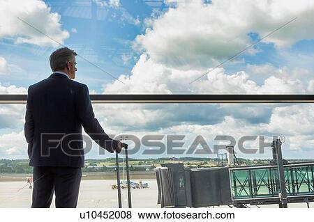 Portrait of mature businessman standing with his suitcase while looking through the window in airport View Large Photo Image Stock Photo - Portrait of mature businessman standing with his suitcase while looking through the window in airport. Fotosearch