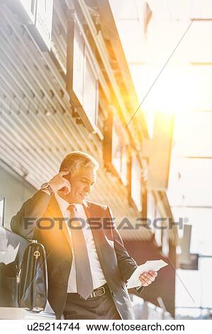Portrait of mature businessman talking on smartphone while looking at his boarding pass in airport View Large Photo Image Picture - Portrait of mature businessman talking on smartphone while looking at his boarding pass in airport. Fotosearch