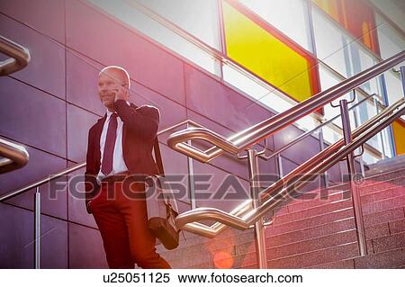 Stock Photography - Portrait of mature businessman talking on smartphone while standing on stairs. Fotosearch