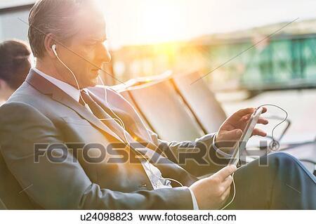 Portrait of mature businessman using digital tablet with earphones on while waiting for boarding in airport View Large Photo Image Stock Image - Portrait of mature businessman using digital tablet with earphones on while waiting for boarding in airport. Fotosearch