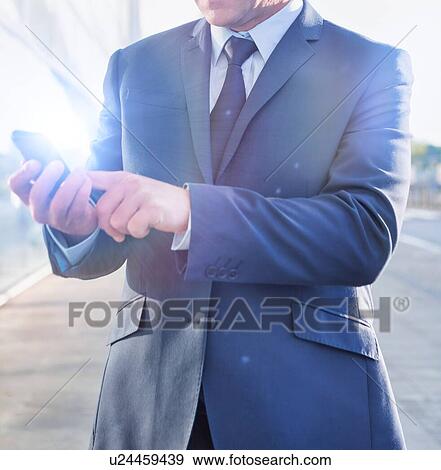 Stock Photo - Portrait of mature businessman using smartphone in airport with lens flare. Fotosearch