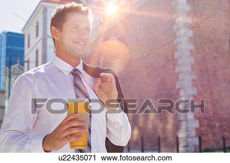 Stock Image - Portrait of mature businessman walking while holding a cup of coffee. Fotosearch
