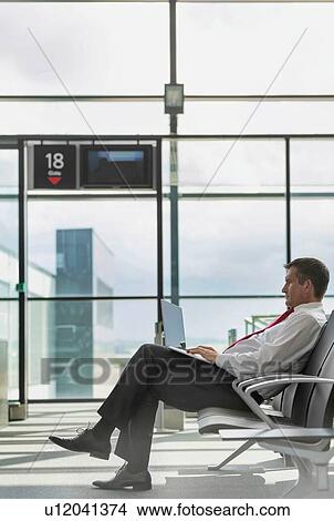 Picture - Portrait of mature businessman working on his laptop while sitting and waiting for flight in airport. Fotosearch