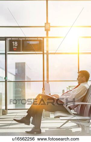 Stock Photograph - Portrait of mature businessman working on his laptop while sitting and waiting for flight in airport. Fotosearch