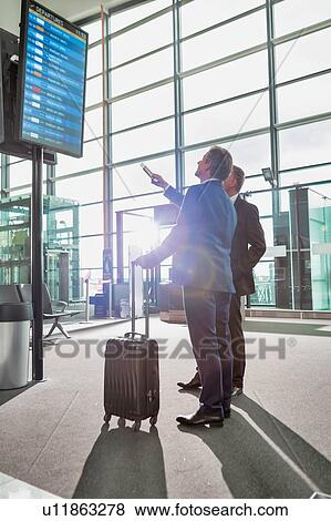Portrait of mature businessmen looking at their flight on monitor in airport View Large Photo Image Stock Photo - Portrait of mature businessmen looking at their flight on monitor in airport. Fotosearch