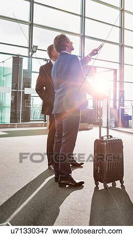Stock Photo - Portrait of mature businessmen looking at their flight on monitor in airport. Fotosearch