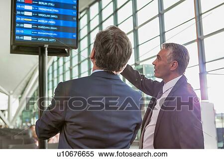 Stock Photography - Portrait of mature businessmen looking at their flight on monitor in airport. Fotosearch