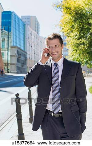 Picture - Portrait of mature confident businessman smiling and talking on smartphone while walking on pavement. Fotosearch