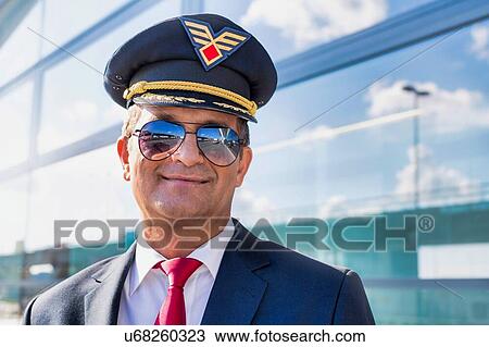 Stock Image - Portrait of mature confident pilot captain wearing eyeglasses in airport. Fotosearch