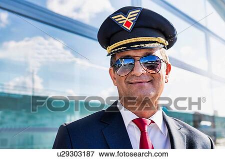 Stock Photo - Portrait of mature confident pilot captain wearing eyeglasses in airport. Fotosearch
