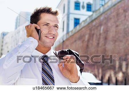 Stock Photo - Portrait of mature confident businessman smiling and talking on smartphone while walking on pavement. Fotosearch