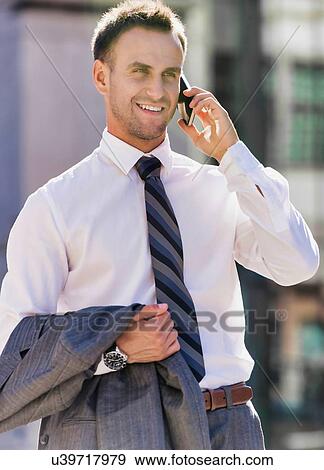 Stock Photo - Portrait of mature confident businessman smiling and talking on smartphone while walking on pavement. Fotosearch