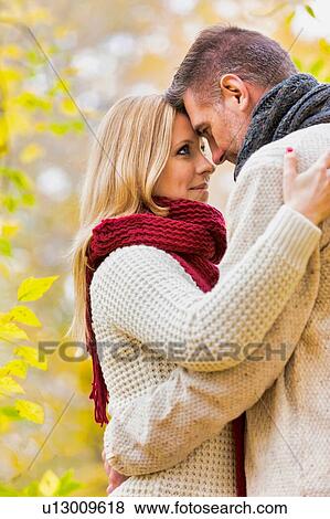 Stock Photo - Portrait of Mature couple enjoying autumn while showing affection in park. Fotosearch