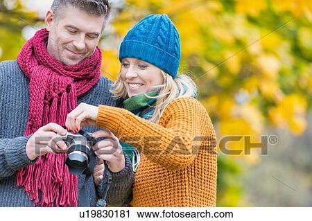 Stock Image - Portrait of mature couple looking pictures on camera in park. Fotosearch