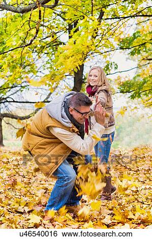 Stock Photograph - Portrait of mature couple playing with maple leaves in park. Fotosearch