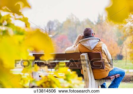 Stock Photograph - Portrait of mature couple sitting on bench while enjoying autumn in park. Fotosearch