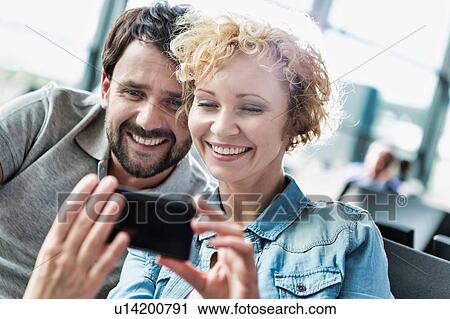 Stock Image - Portrait of mature couple taking and looking at their selfie while waiting for boarding in airport. Fotosearch