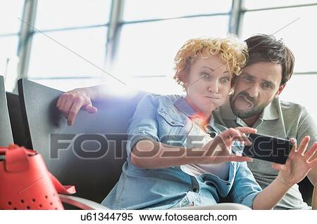 Stock Photography - Portrait of mature couple taking selfie while waiting for boarding in airport. Fotosearch