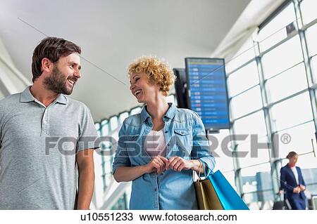 Stock Image - Portrait of mature couple walking while talking in airport. Fotosearch